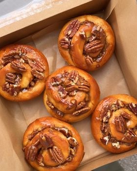 Five caramel pecan brioche rolls topped with pecan halves in a cardboard box, seen from above