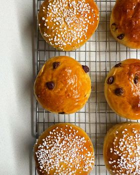 Round brioche buns topped with chocolate chips, and others with pearl sugar, cooling on a wire rack