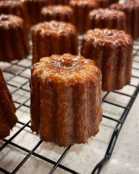 Glossy caramelised canelés on a wire cooling rack, close up