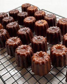 About twenty canelés in rows on a black wire cooling rack