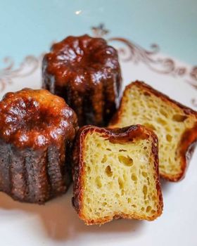 Three canelés on a floral-rimmed plate, one cut in half to show the custard inside