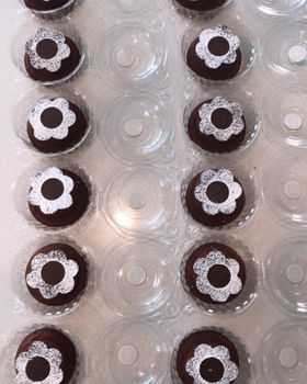 Chocolate fondants dusted with a powdered sugar flower, each in a clear tray well, seen from above