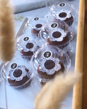 Chocolate fondants with powdered sugar flowers in clear clamshell boxes on a tray, dried wheat stems in front