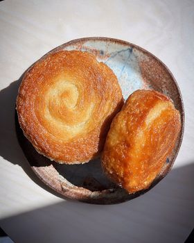 A large swirled kouign amann and a smaller one on a speckled ceramic plate