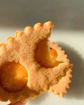Fingers hold an apricot jam lunette with a bite taken out of it
