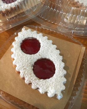 A strawberry jam lunette dusted with powdered sugar on a sheet of parchment in a clear box