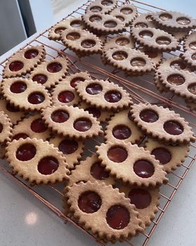 Dozens of lunette cookies with strawberry and apricot jam windows cooling on a copper wire rack