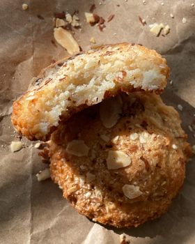 An almond macaron broken in half showing its soft interior, with sliced almonds on brown parchment