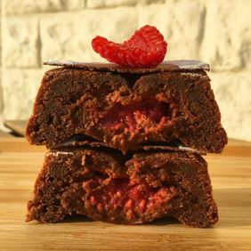 Two stacked chocolate raspberry fondants cut open to show a molten raspberry centre, topped with a raspberry