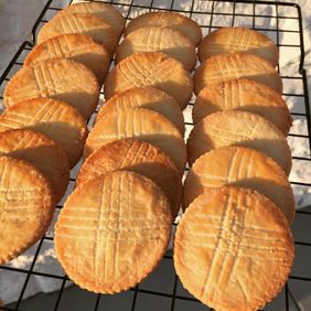 Rows of round butter galettes with a crosshatch pattern cooling on a wire rack in sunlight