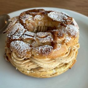 A Paris-Brest choux ring filled with praline cream, topped with sliced almonds and powdered sugar, on a white plate