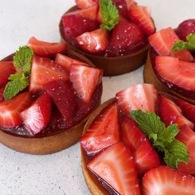 Four strawberry tartlets topped with cut strawberries and mint leaves