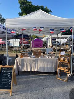 The GM Petit Cafe market tent with French flag bunting, a table of packaged pastries, a wooden display ladder and a chalkboard menu