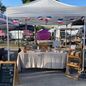 The GM Petit Cafe market tent with French flag bunting, a table of packaged pastries, a wooden display ladder and a chalkboard menu