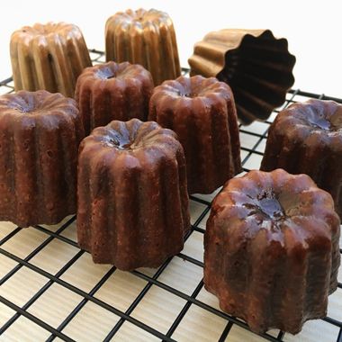 Seven canelés on a wire rack with three copper canelé moulds behind them
