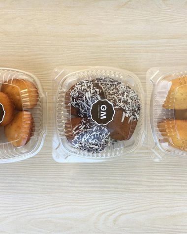 Three clear takeout containers of madeleines and financiers on a wooden table on a delivery day