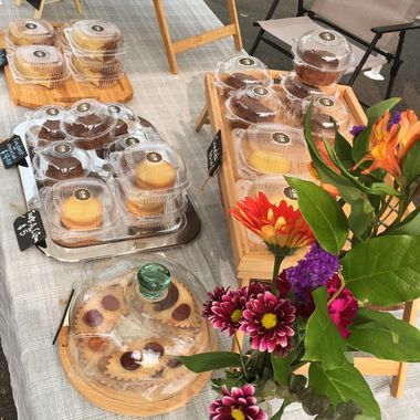 A market table with clamshell boxes of pastries, chalkboard price tags and a vase of flowers