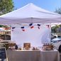 A white canopy hung with French flag bunting over a market table of pastries under a blue sky