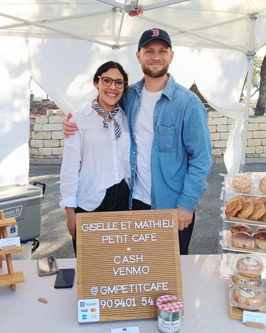 A woman and a man smile under the market tent behind shelves of packaged pastries at the Downtown Georgetown Christmas Stroll