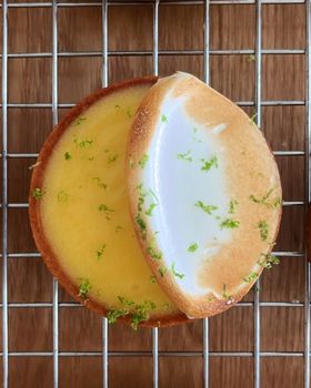 Two lemon meringue tarts with toasted meringue and lime zest on a wire rack